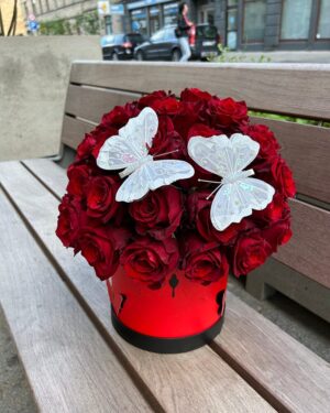 Sarkanas rozes apaļā kastē ar tauriņiem